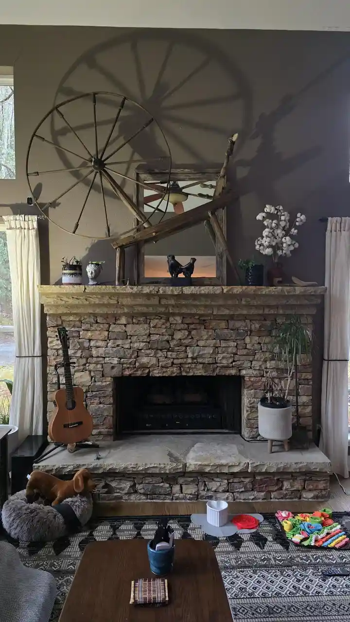 A cozy living room features a stone fireplace with rustic decor, including a large wagon wheel mounted on the wall above it…