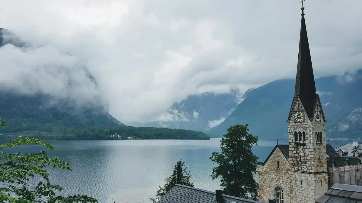 Hallstatt's iconic lakeside church stands majestically, reflected perfectly in the mist-shrouded water. Towering mountains…