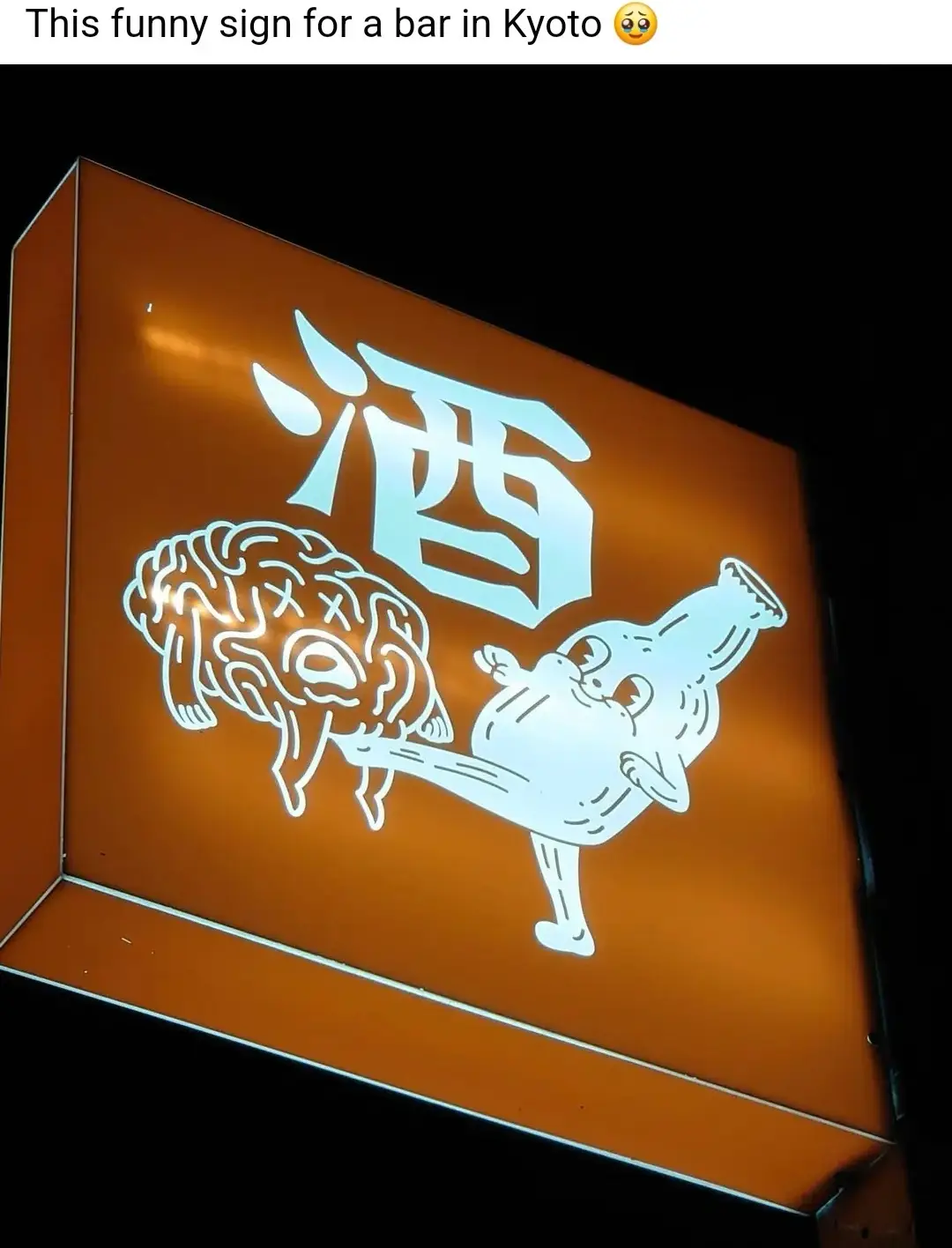An illuminated orange sign features a large Japanese kanji character for 'sake' (酒) above a cartoon bottle character kicking…