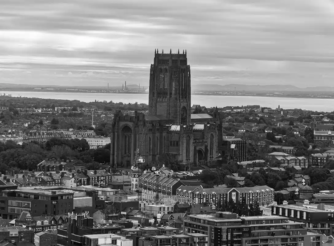 A black-and-white photo shows a large Gothic cathedral dominating a cityscape, with construction equipment visible near its…