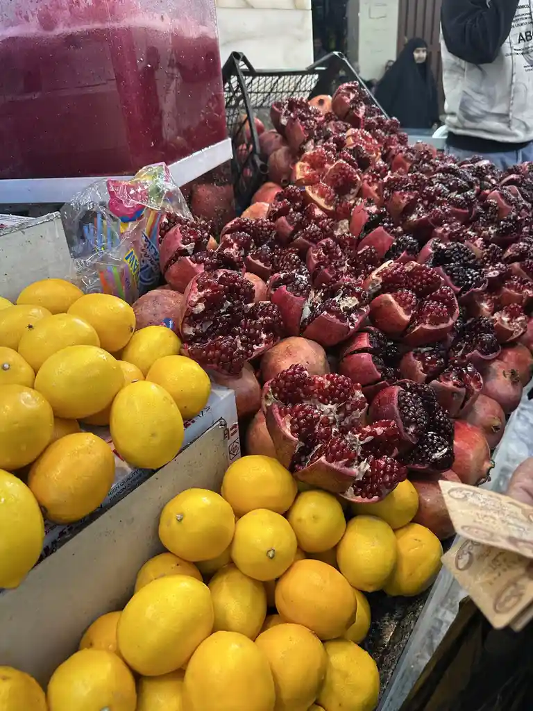 A vibrant fruit stall displays piles of bright yellow lemons and numerous pomegranates cut open to reveal their juicy red…