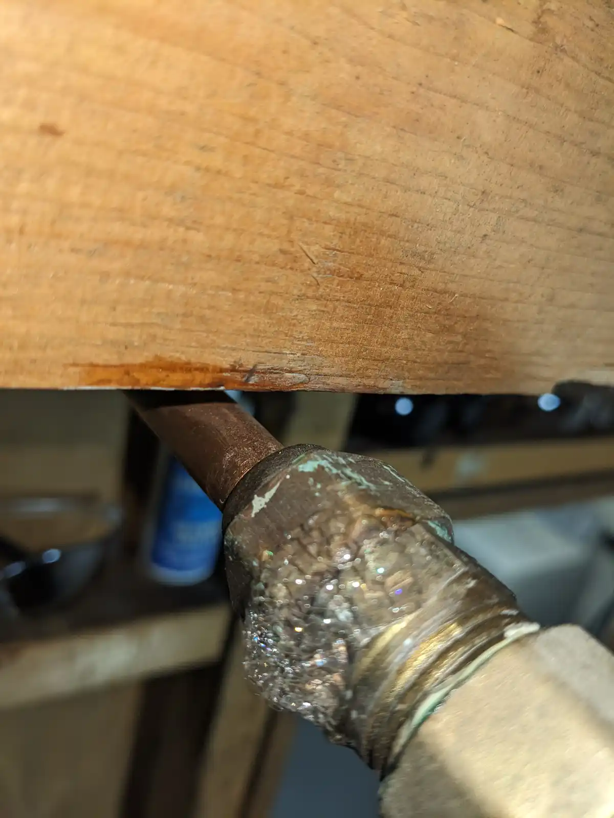 A close-up photo shows a copper pipe with a hexagonal fitting underneath a wooden table, covered in sparkling glitter. The…