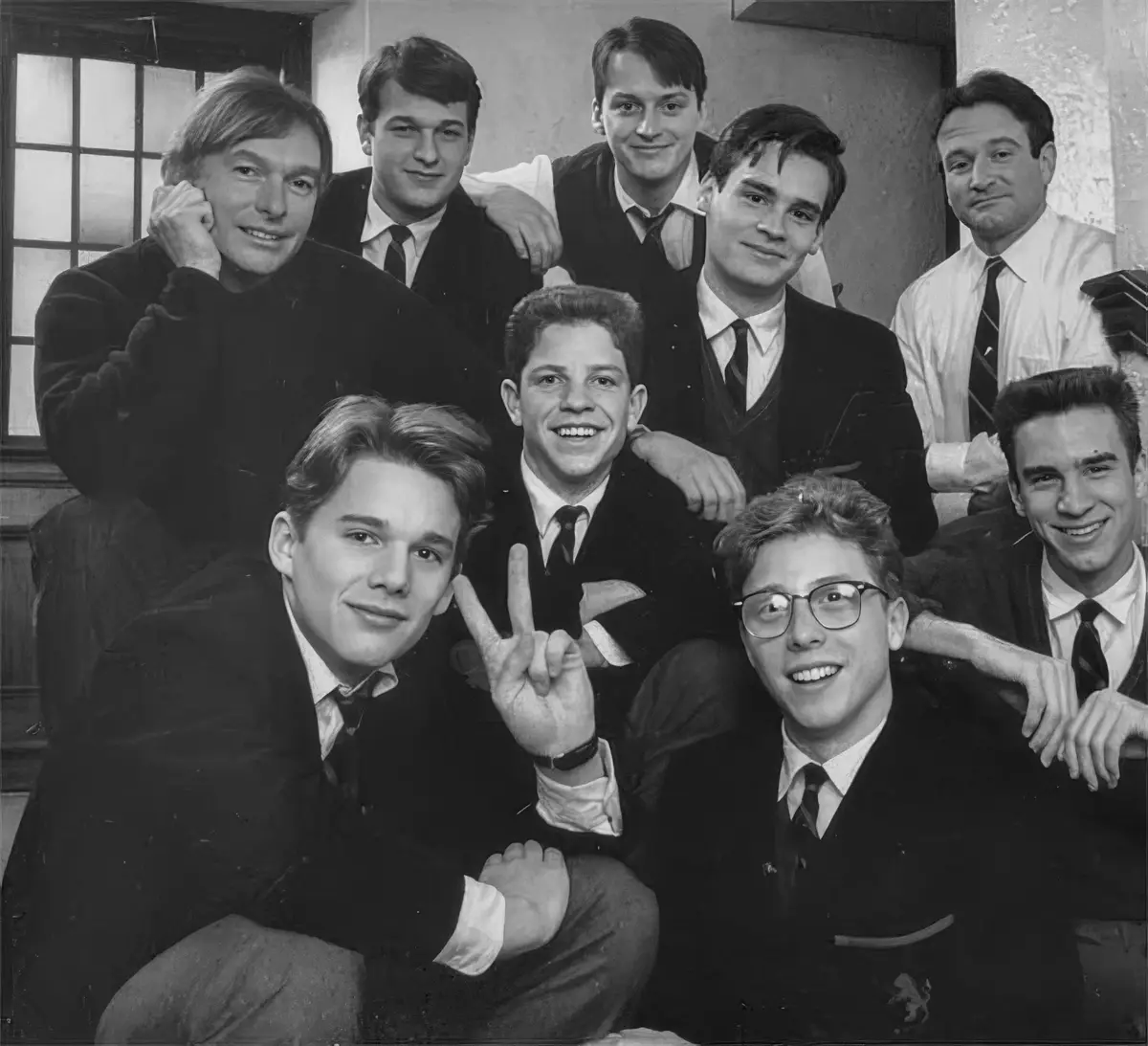 A black-and-white group photo of eight young men in school uniforms posing together. One man in the front row, wearing…