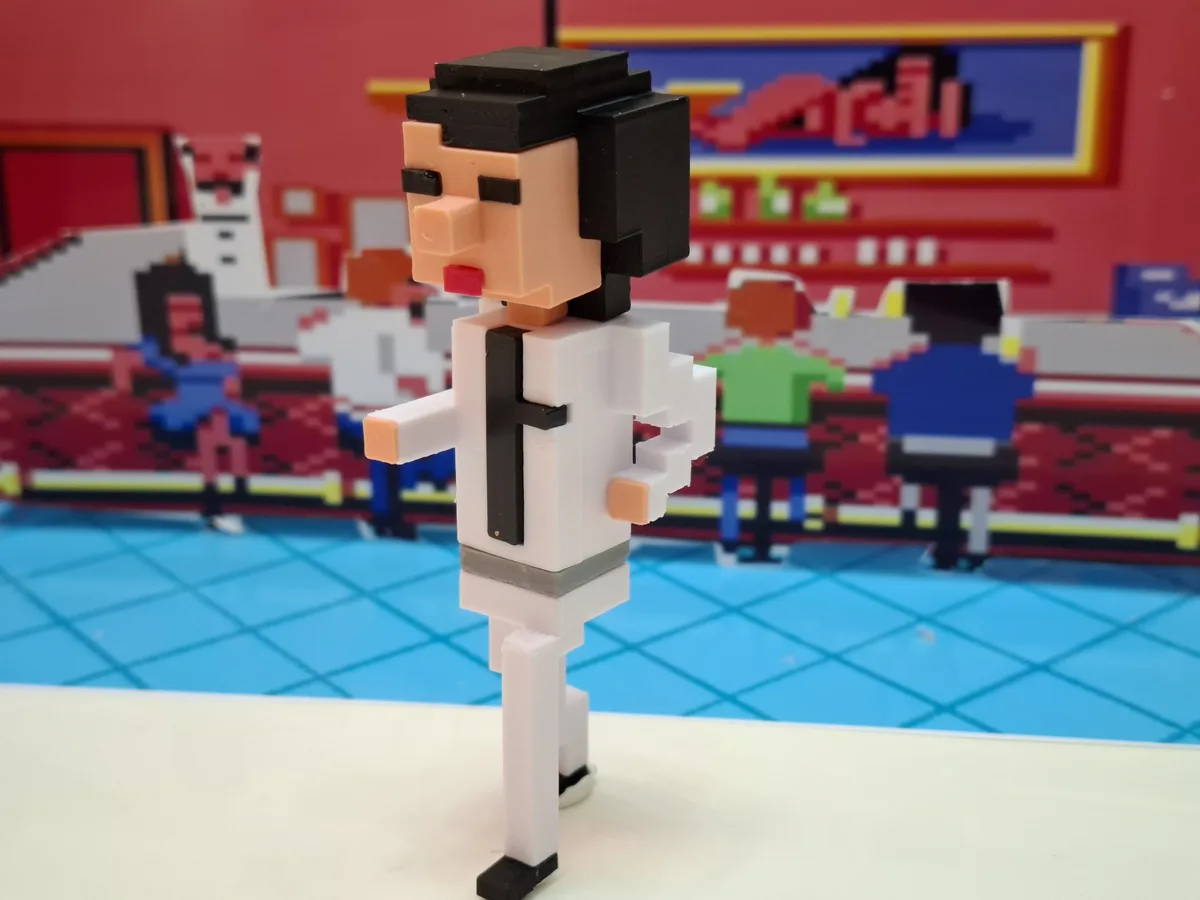 A 3D-printed pixel-art figure of a man in a white lab coat and black tie stands in front of a pixelated classroom scene with…