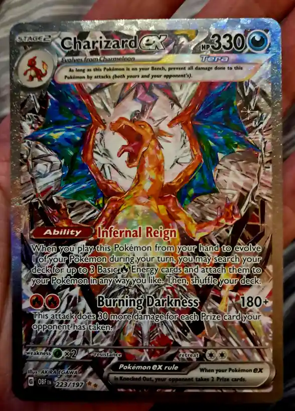 A hand holds a shiny Pokémon TCG card of Charizard EX with 330 HP, featuring an artistic, fragmented illustration of the…