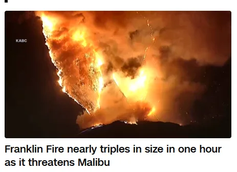 A dramatic nighttime shot shows a massive wildfire with bright orange flames and thick smoke billowing upwards, illuminating…