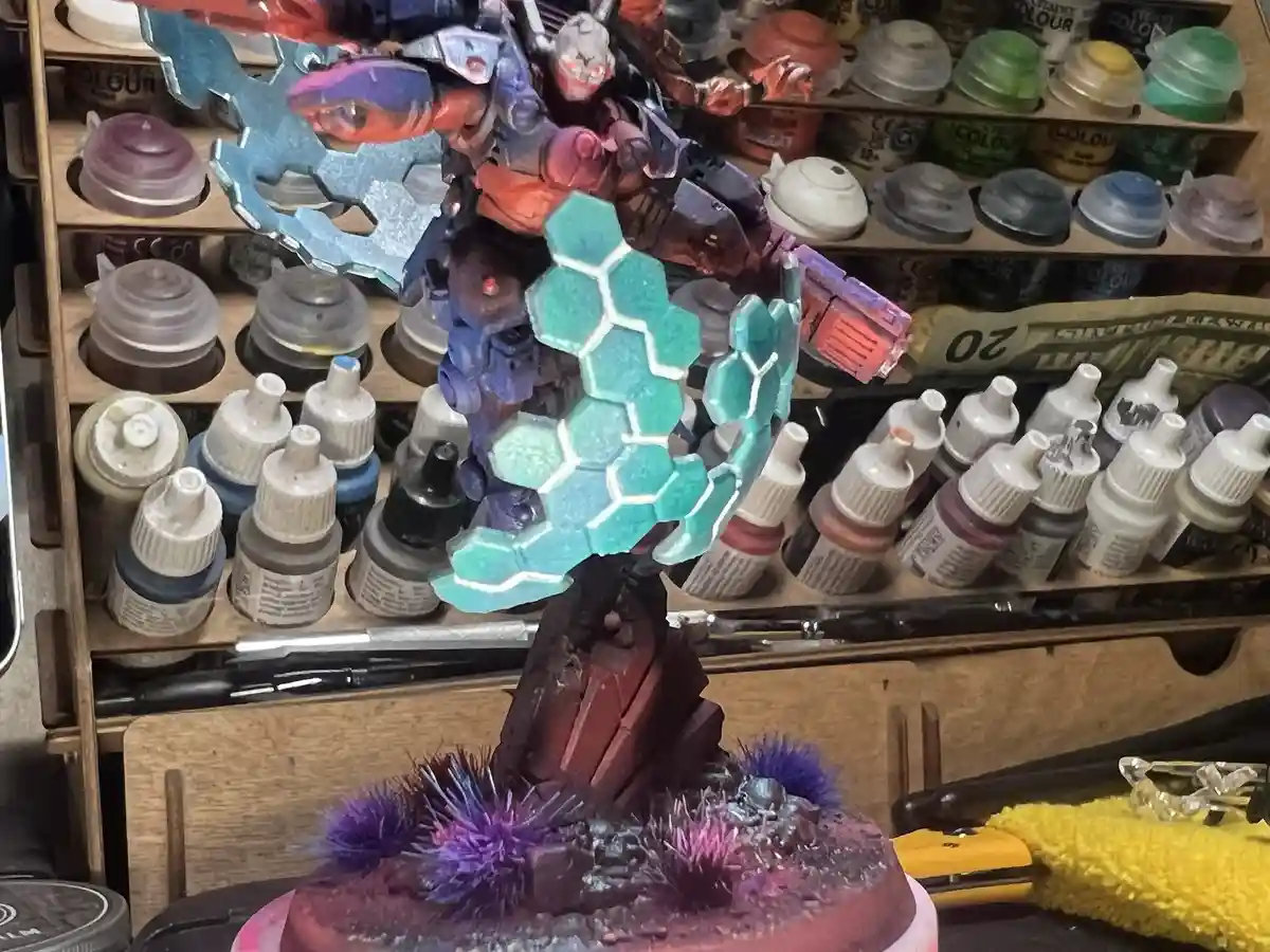 A highly detailed, painted miniature model of a sci-fi character with glowing blue hexagonal armor stands on a rocky base…