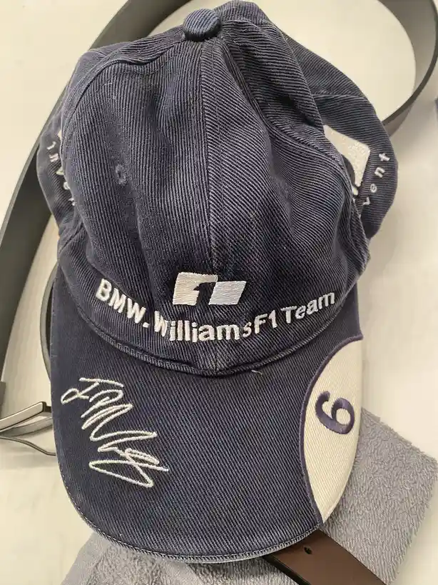 A navy blue baseball cap with white embroidery reading 'BMW.WilliamsF1 Team' and a stylized 'F1' logo, featuring a white…