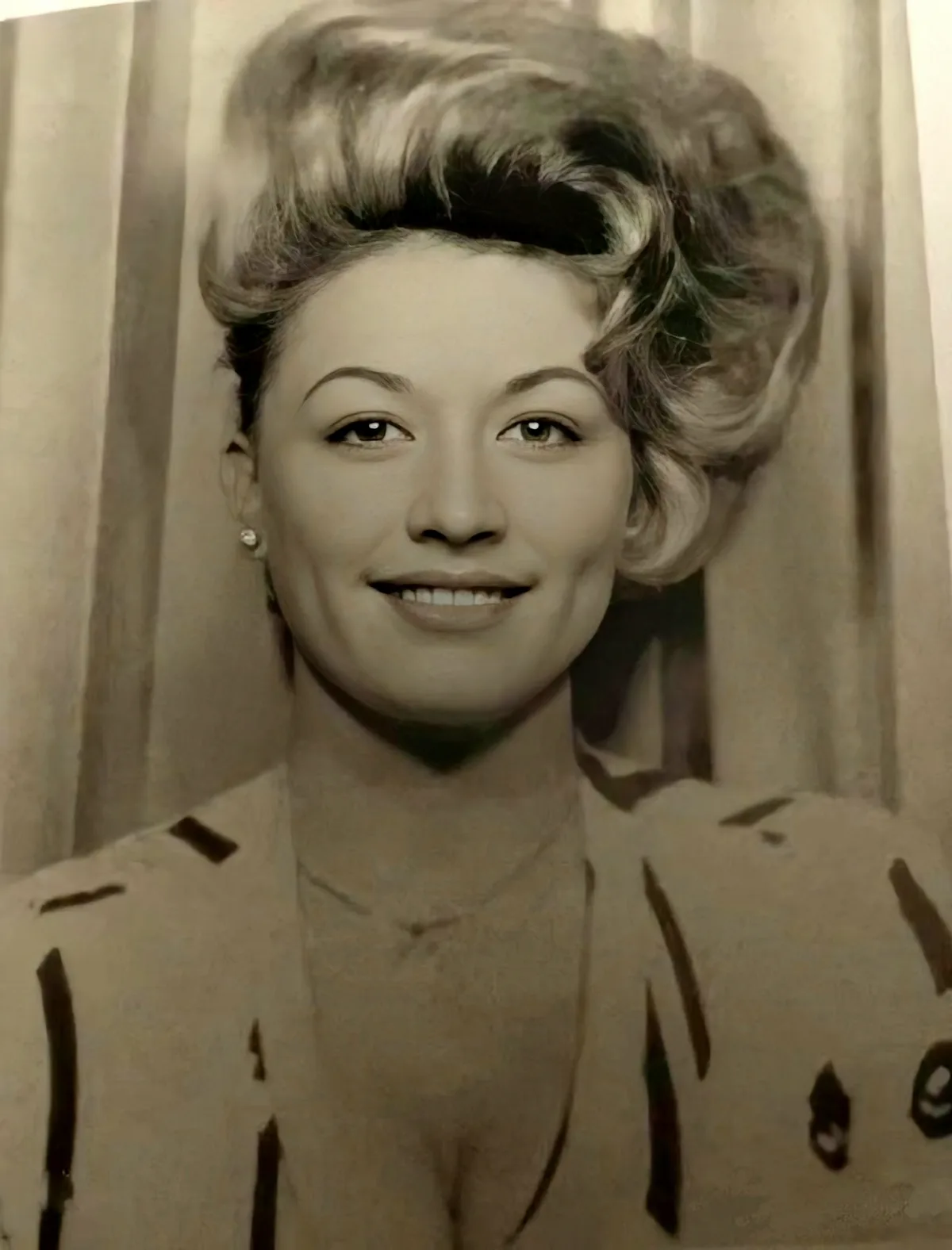 A vintage sepia-toned portrait of a smiling woman with styled hair and pearl earrings, wearing a patterned blouse against a…