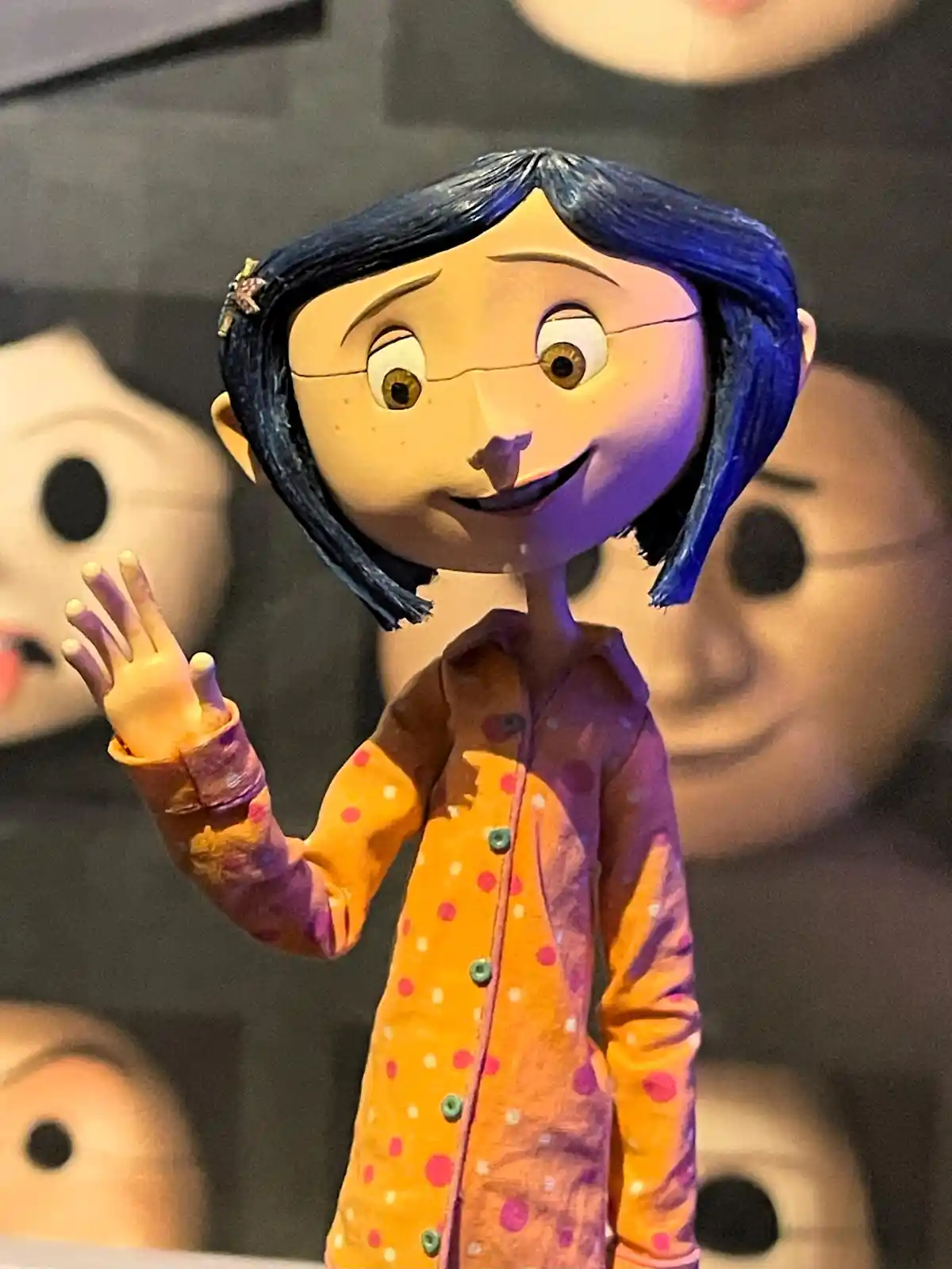 A close-up of a figurine of the animated character Coraline, who has blue bobbed hair, freckles, and is wearing a colorful…