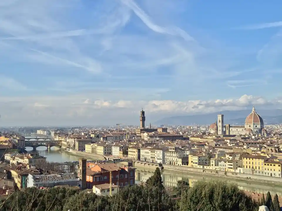 A scenic panoramic view of Florence, Italy, showing the Arno River, historic buildings, the Duomo with its iconic dome, and…
