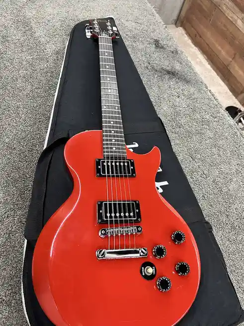 A bright red electric guitar with a black pickguard and chrome hardware rests on a black guitar case, which is lying on a…