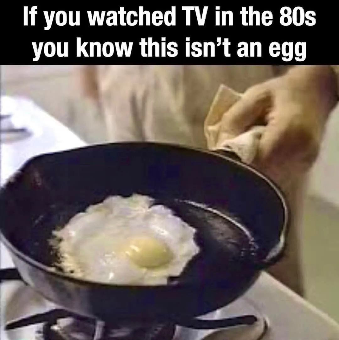A close-up shot of a fried egg in a black frying pan on a stovetop, with a hand holding a cloth near the pan's handle. The…