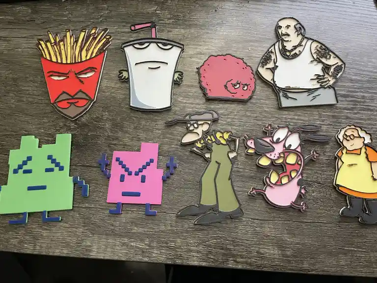 Several 3D-printed character cutouts, including a french fry face, a drink cup, a pink blob, a muscular man, pixelated green…