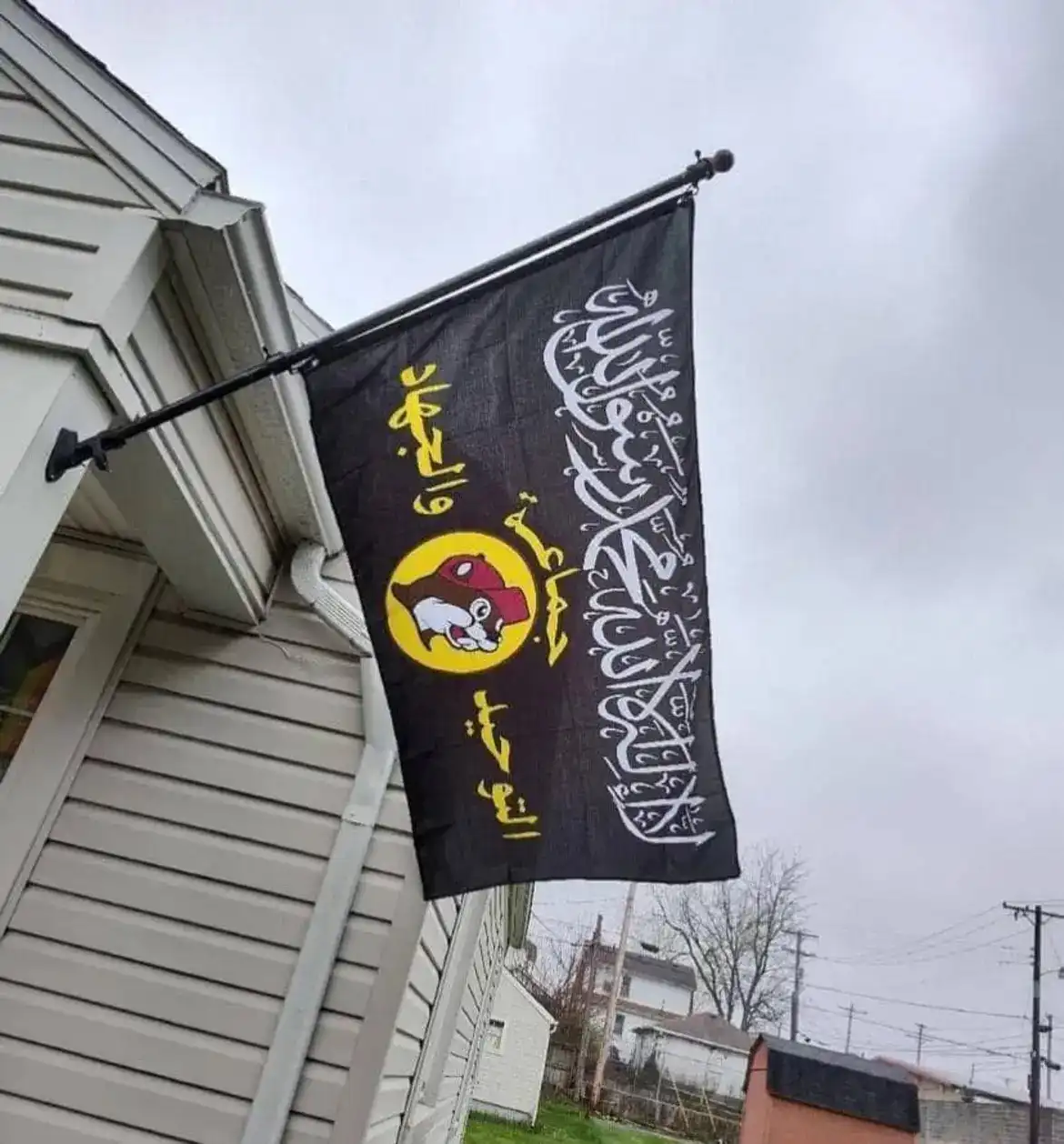 a black flag attached to a house's exterior flagpole displays white arabic calligraphy and a yellow circle containing a…