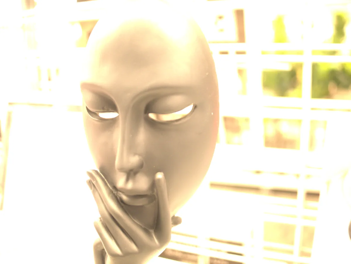 A close-up of a serene, featureless gray mannequin head with closed eyes and a hand gently resting near its mouth, set…