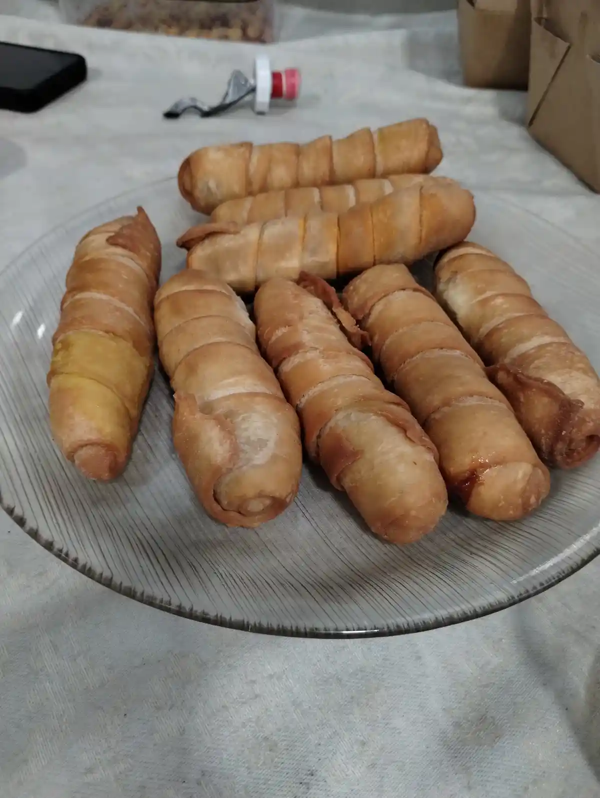 A plate of golden-brown, segmented fried spring rolls sits on a patterned glass plate. The text overlay reads 'i made these…