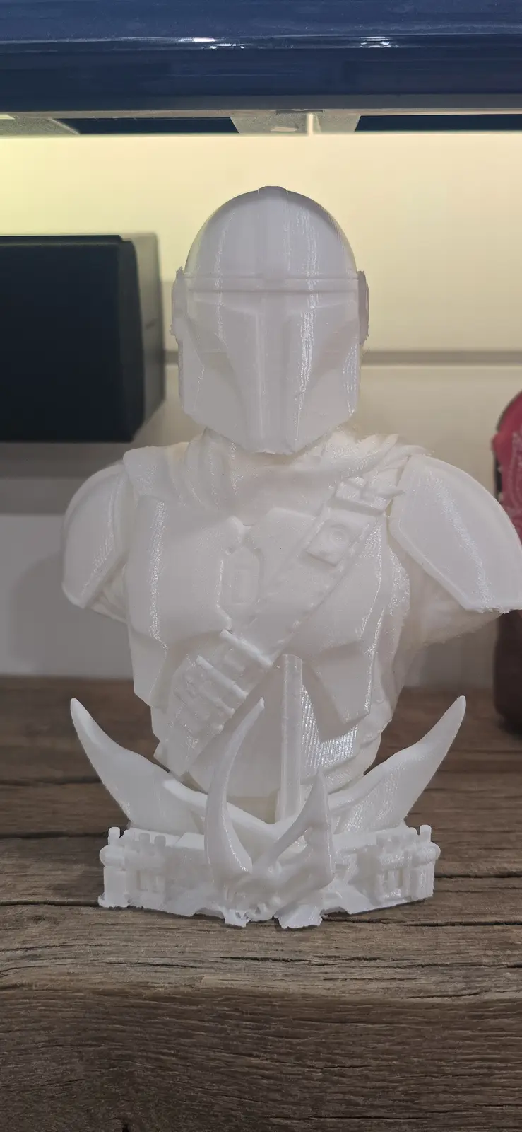 A white 3d-printed bust of The Mandalorian from Star Wars, standing on a base with two curved horns and a small castle-like…