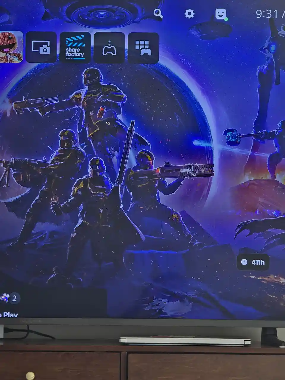 A screenshot of a TV screen showing a video game's home interface with a space-themed wallpaper featuring four armored…