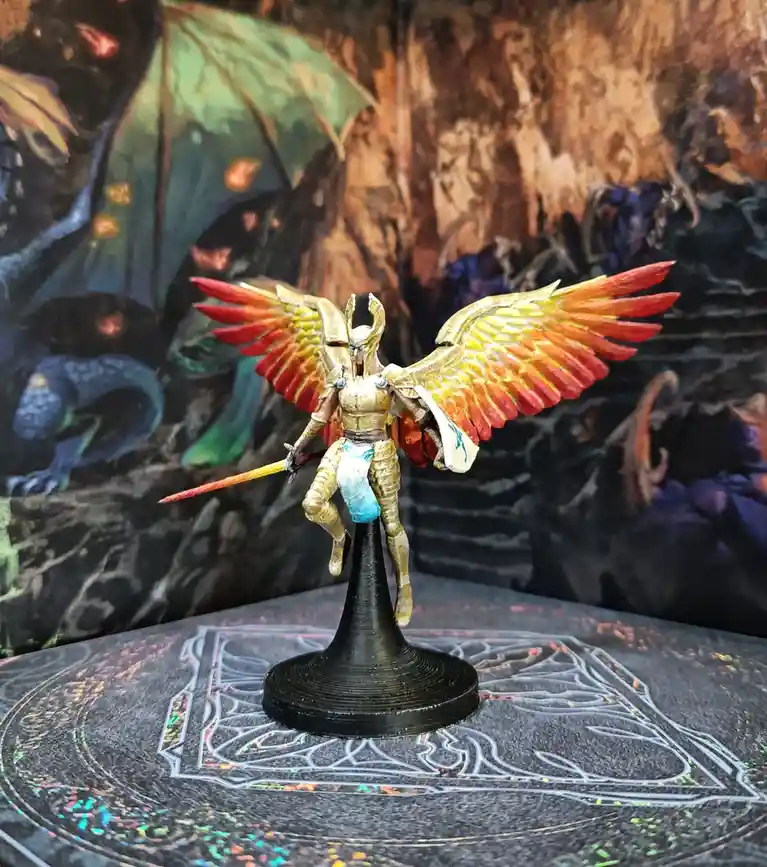 A painted miniature figurine of a humanoid warrior with large, colorful wings (red, orange, yellow) and a horned helmet…