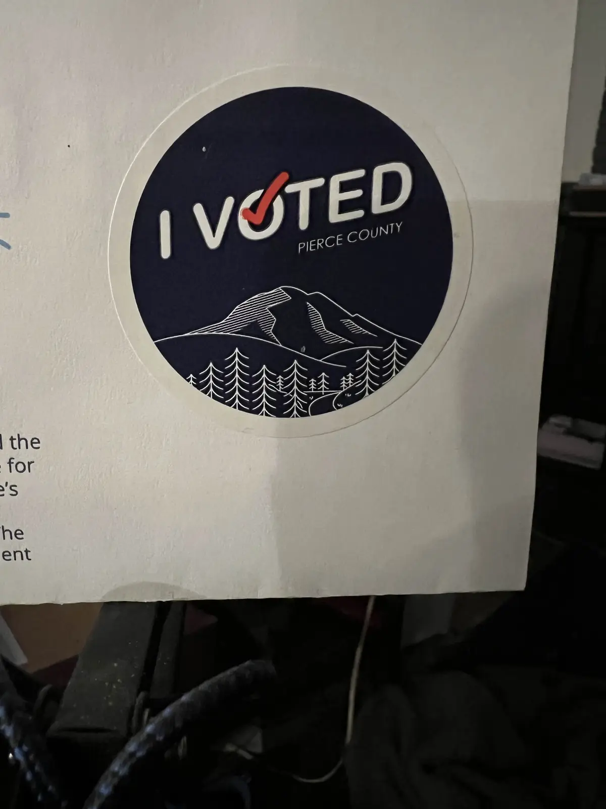 A circular dark blue 'I VOTED' sticker from Pierce County is stuck on a white surface, featuring a white line drawing of…
