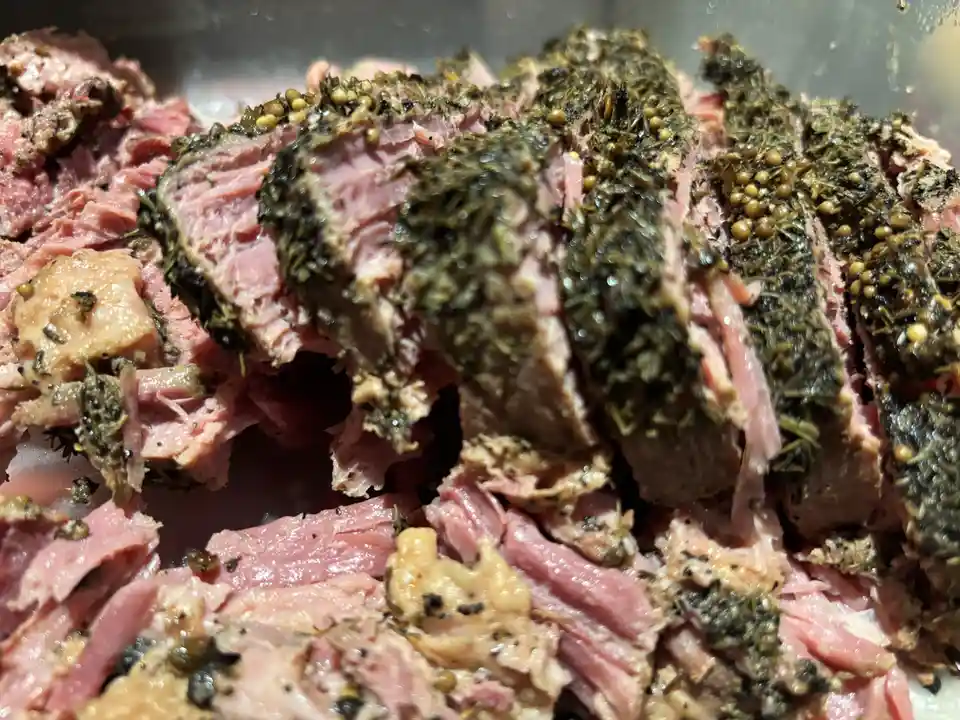 A close-up photo shows sliced roast beef with a dark, herb-and-seed crust, revealing pink, juicy interior meat. The overlaid…