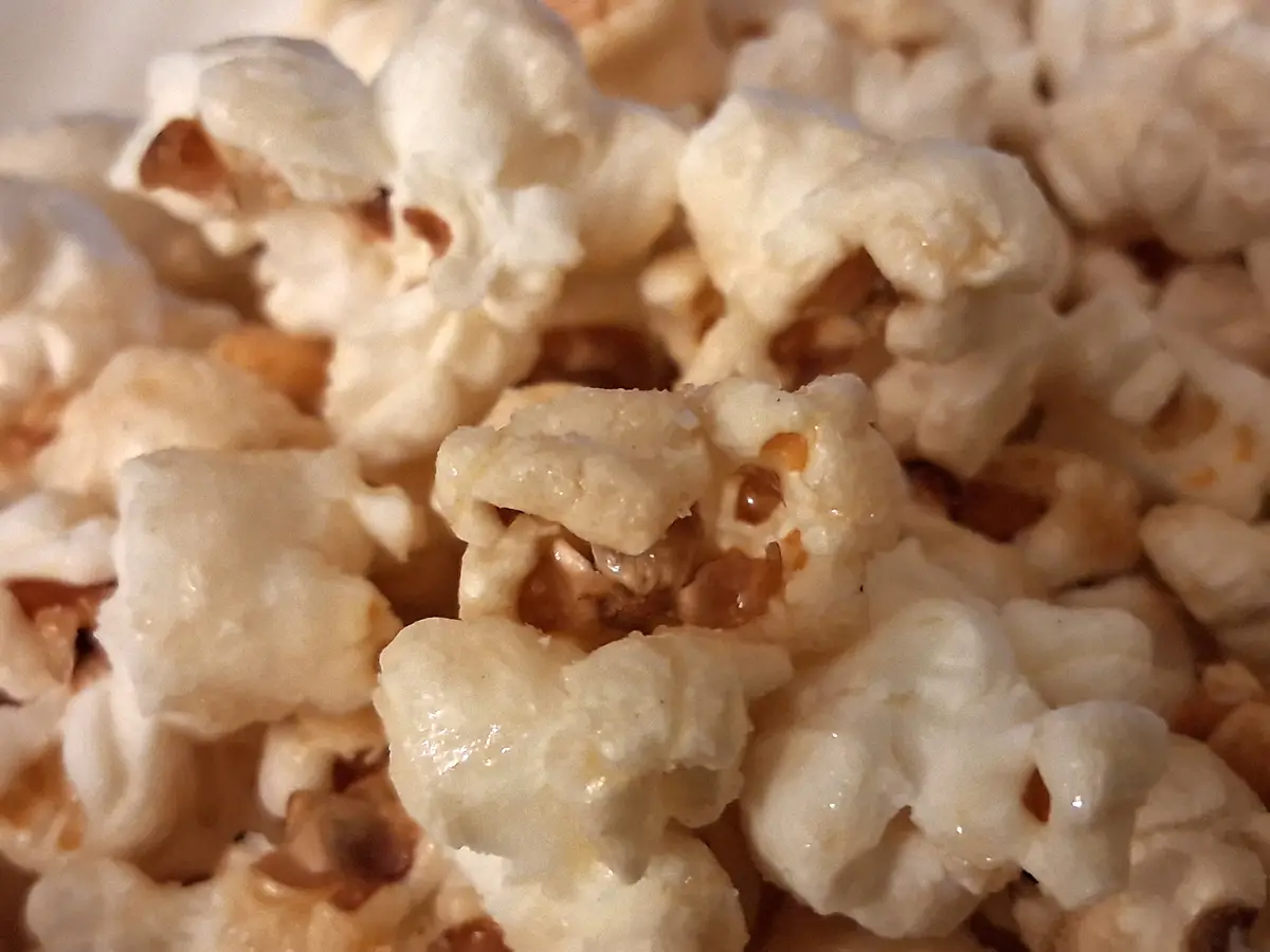 A close-up photo shows a pile of caramel popcorn, with individual popped kernels coated in glossy, amber-colored caramel…