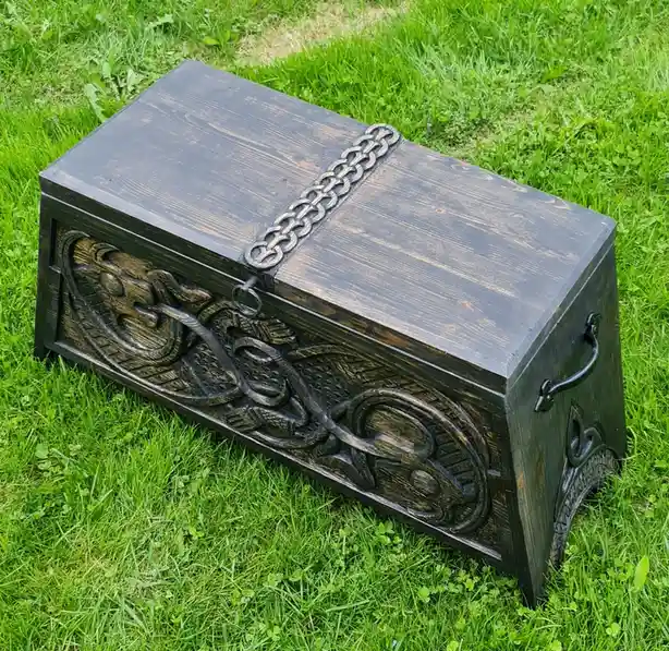 A dark wooden chest with ornate carvings and a metal chain strap sits on green grass. The overlaid text reads 'my dad's new…