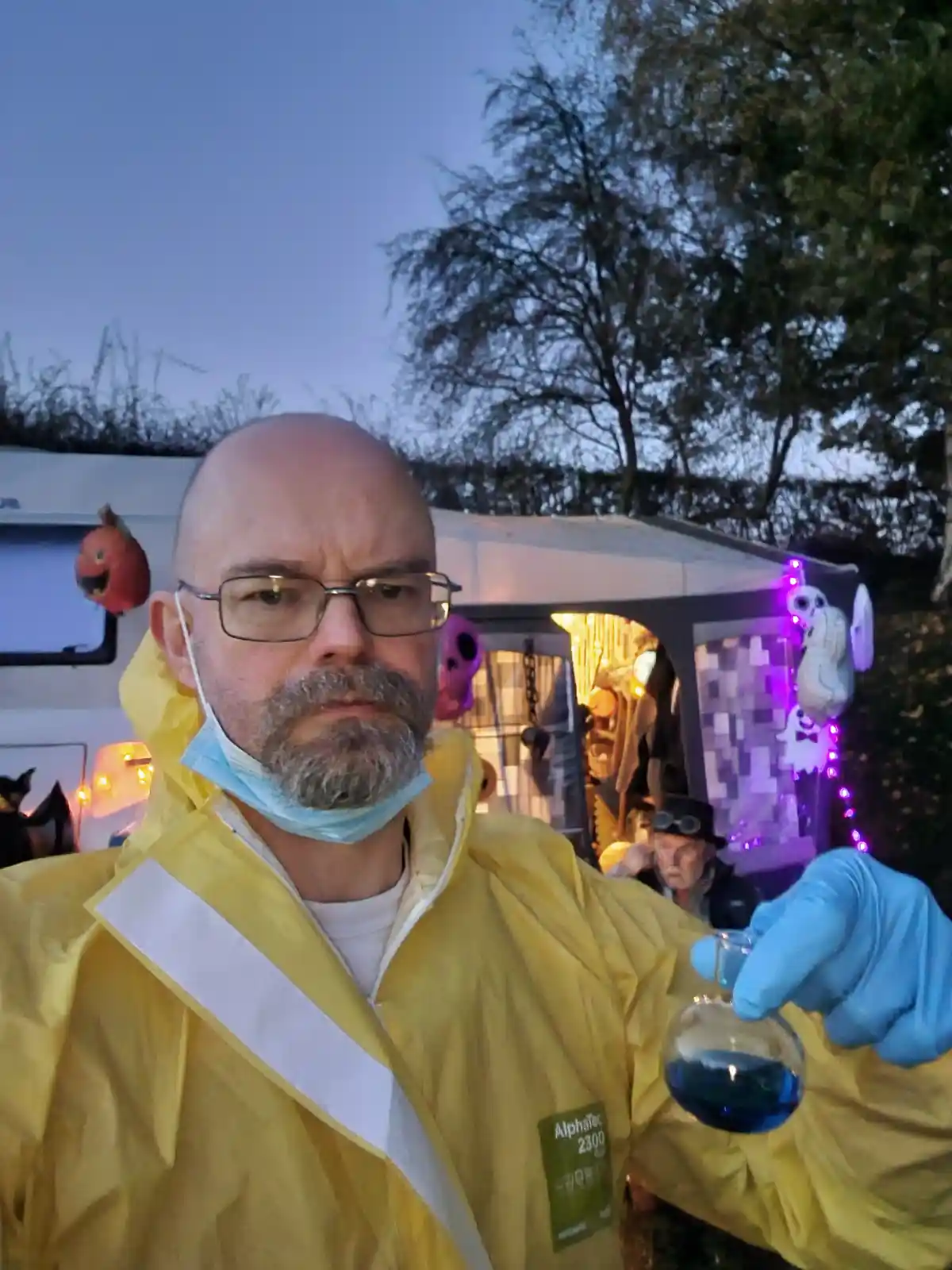 A man with glasses and a goatee, wearing a yellow hazmat-style jacket with a name tag reading 'AlphaTec 2300', blue nitrile…