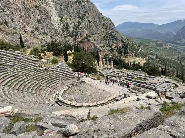 this is a wide-angle photograph of the ancient theater of epidauros, showing its iconic semi-circular stone seating tiers…