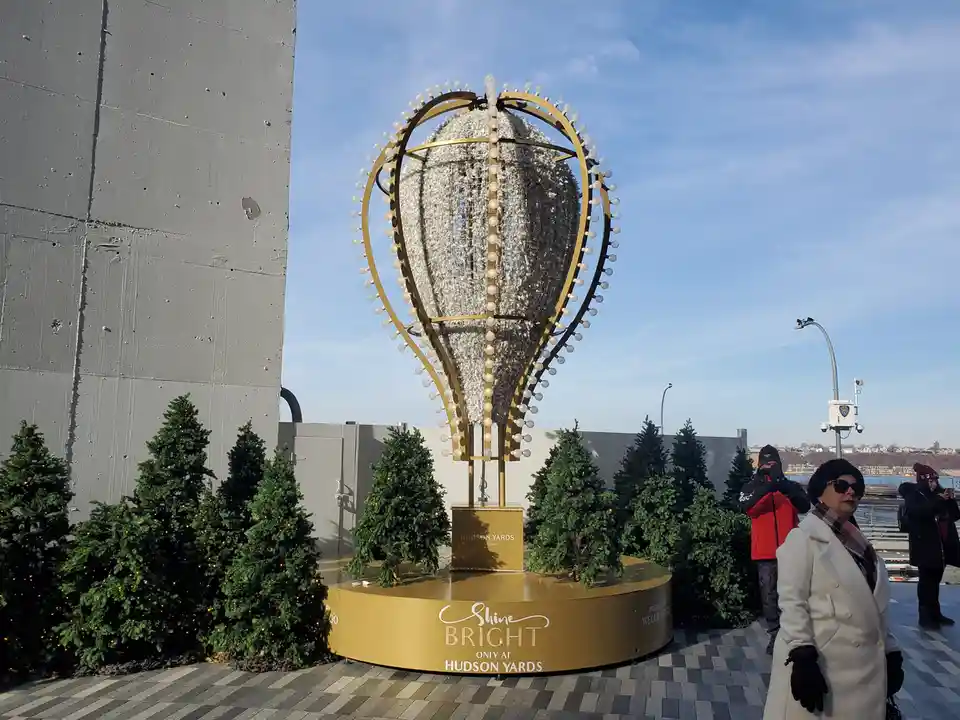 A large, ornate golden hot air balloon sculpture adorned with white lights and a glittery silver interior stands on a…