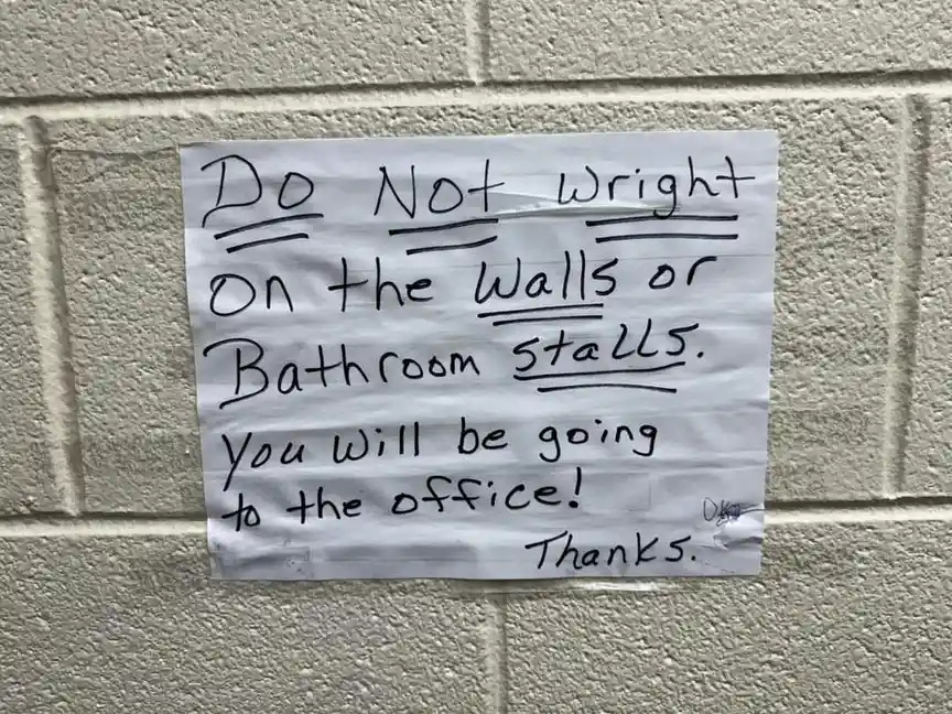 A handwritten note on crumpled paper taped to a beige cinder block wall reads 'Do Not Wright On the Walls or Bathroom…