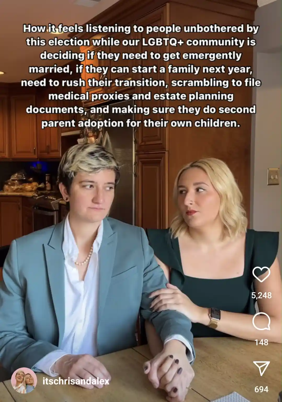 Two people sit at a kitchen table, holding hands, with one looking away with a weary expression and the other looking at…