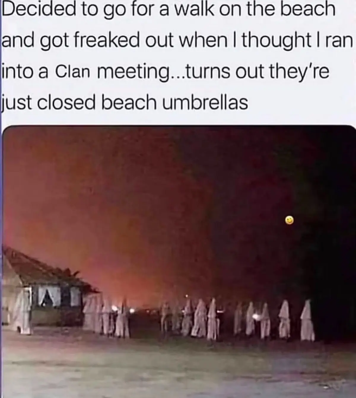 A low-resolution nighttime photo shows a row of closed, light-colored beach umbrellas standing upright on sand, creating a…