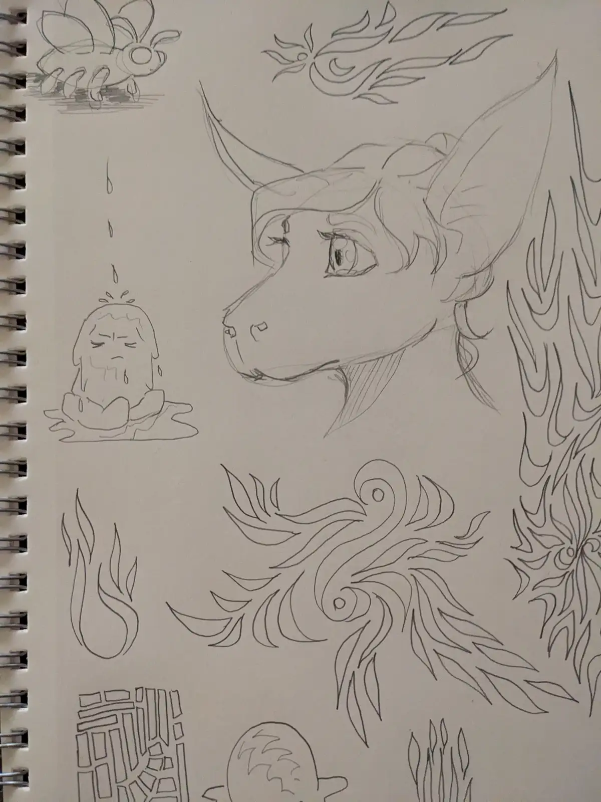 A sketchbook page shows various pencil drawings including a large dragon head, a crying cartoon character, and abstract…
