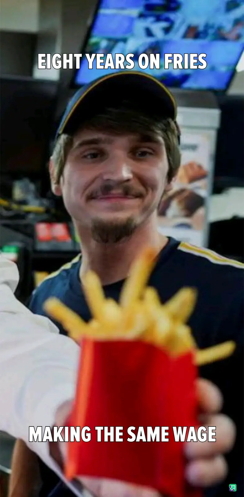 A man in a dark cap and blue shirt smiles while holding a red paper container of french fries, with text overlaid at the top…