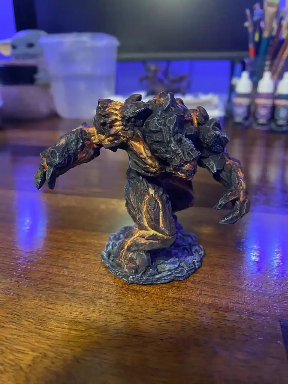A hand-painted miniature figurine of a monstrous, rocky creature with glowing orange lava-like details stands on a wooden…