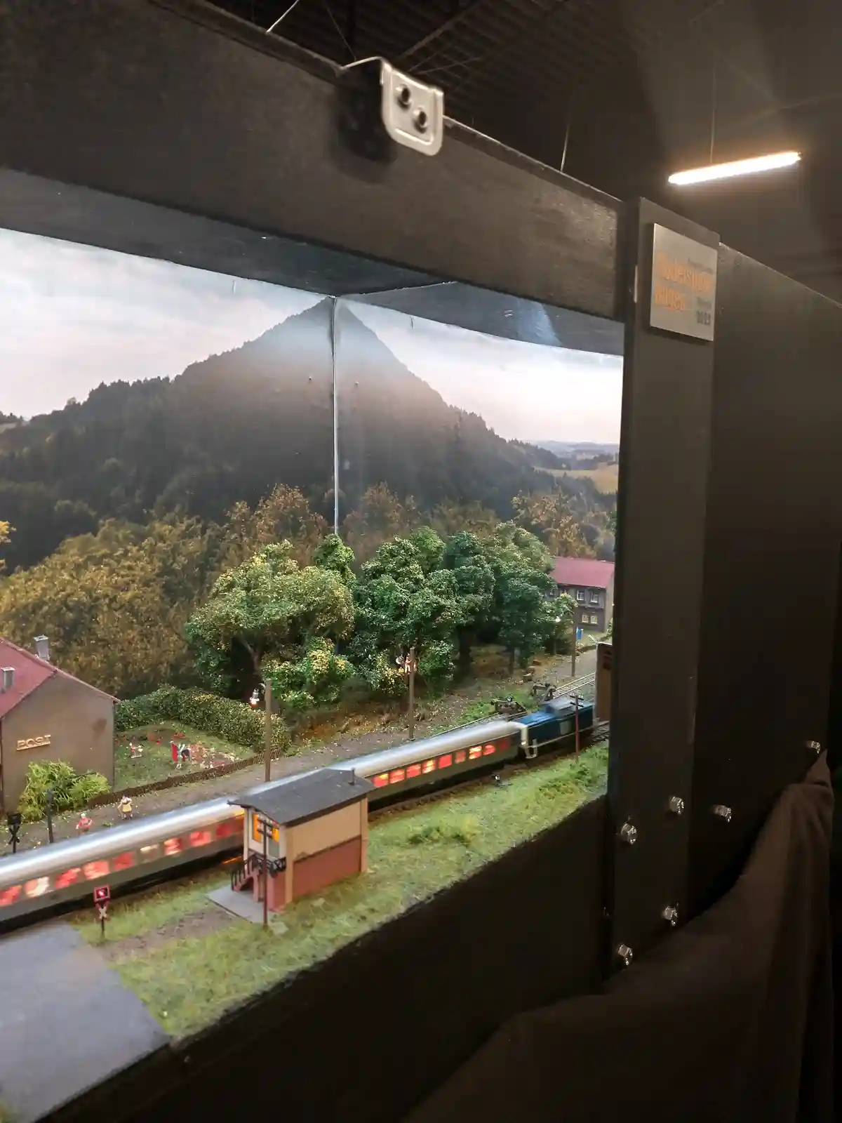 A photograph of a detailed model train diorama displayed in a glass case, featuring a miniature train with glowing red…