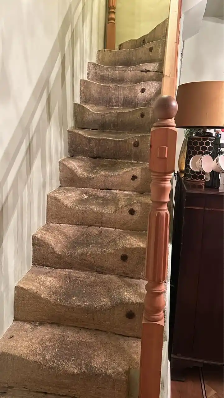 A close-up photo of a staircase with worn, uneven stone steps that appear aged and weathered, flanked by a wooden banister…