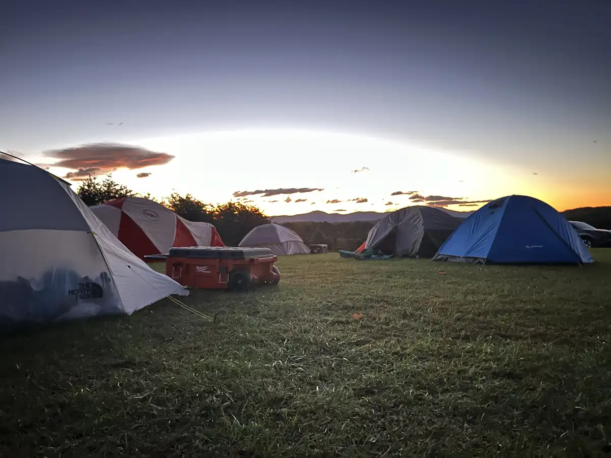 A serene campsite at sunset with multiple tents of various colors and brands, including The North Face, set on a grassy…