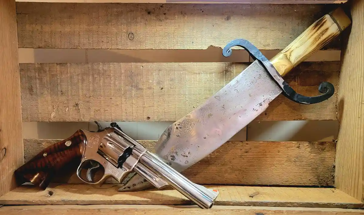 A shiny silver revolver with a wooden grip lies next to a large, rustic knife with a bone handle and ornate black metal…