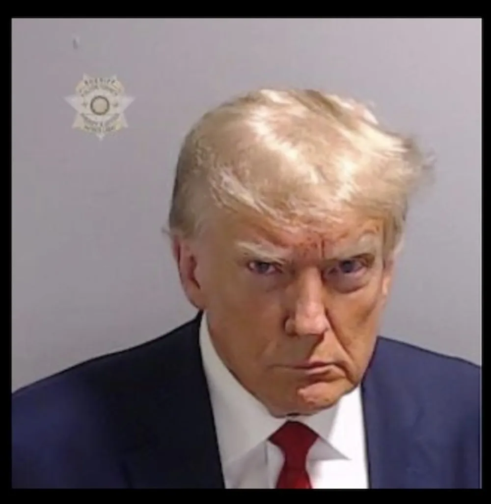 A mugshot-style photo of Donald Trump with a stern expression, wearing a dark suit and red tie, against a plain gray…
