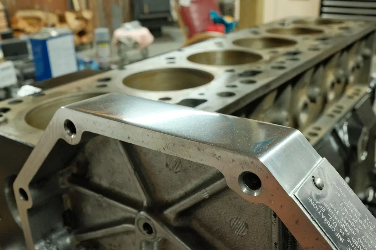 A close-up photo of a shiny, freshly machined engine block with visible cylinder bores and bolt holes, set against a blurred…
