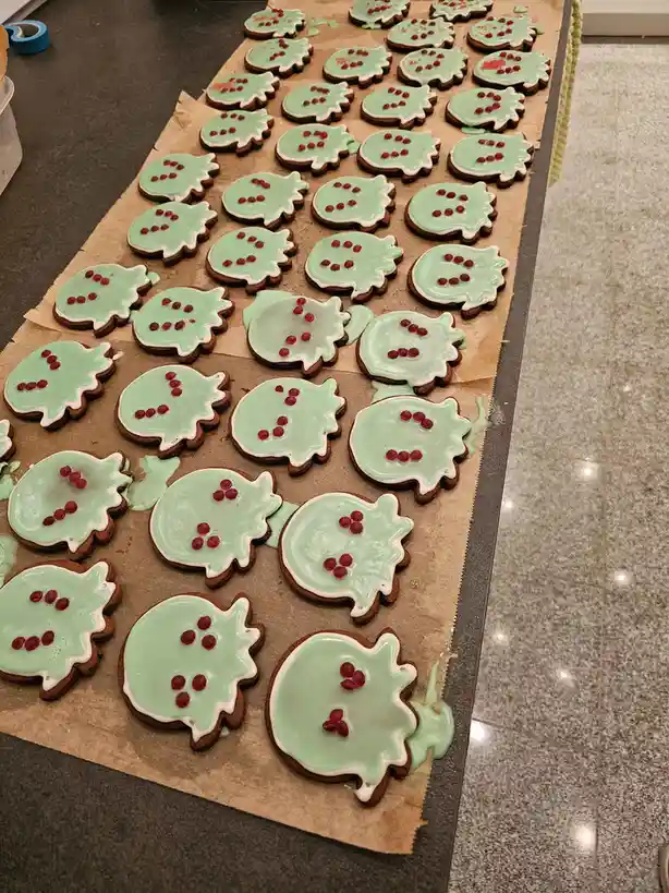 A long row of gingerbread cookies shaped like pomegranates, covered in light green icing and decorated with red dots…