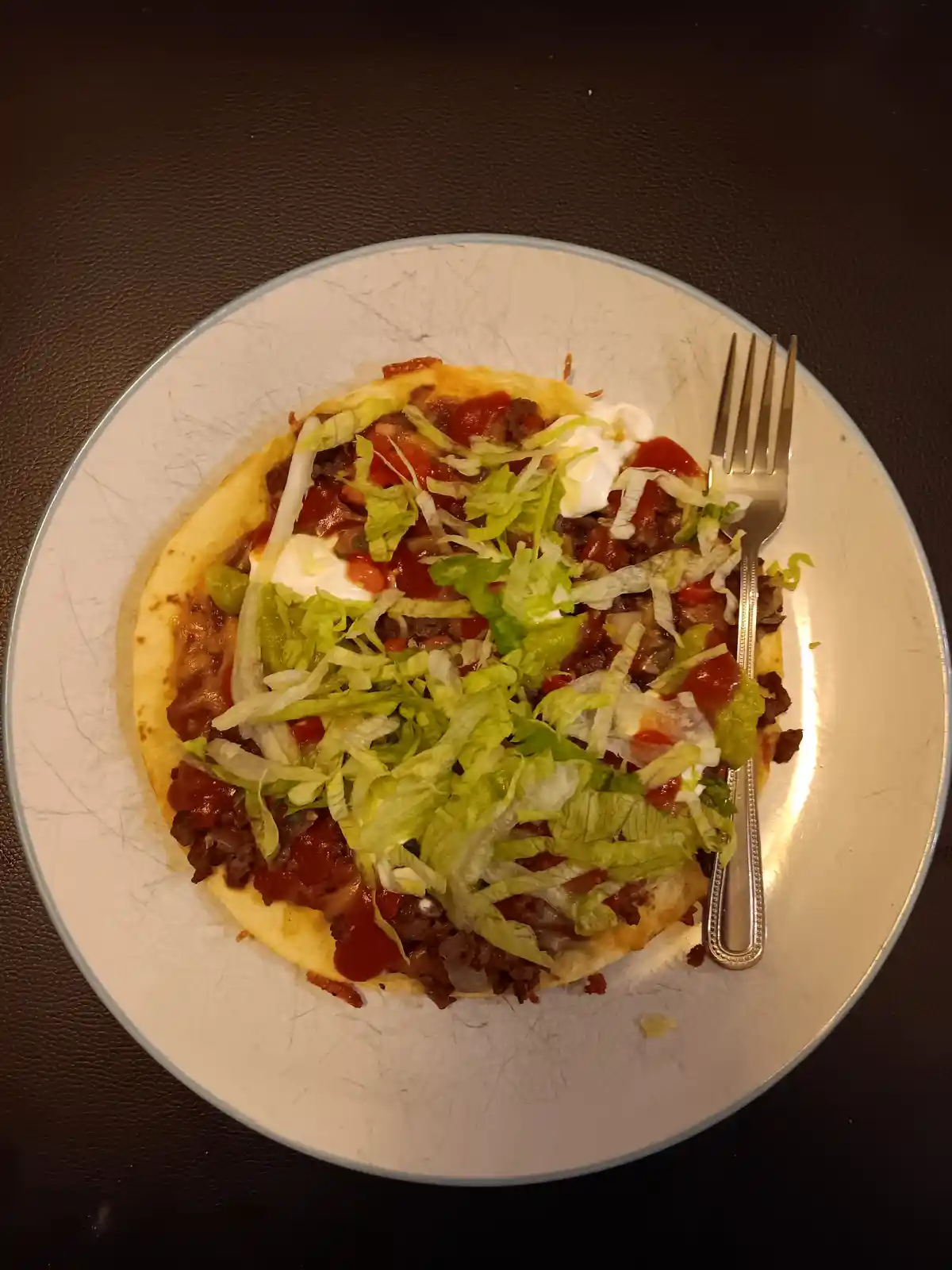 A close-up photo shows a single, round, soft tortilla on a white plate, generously topped with shredded lettuce, red sauce…