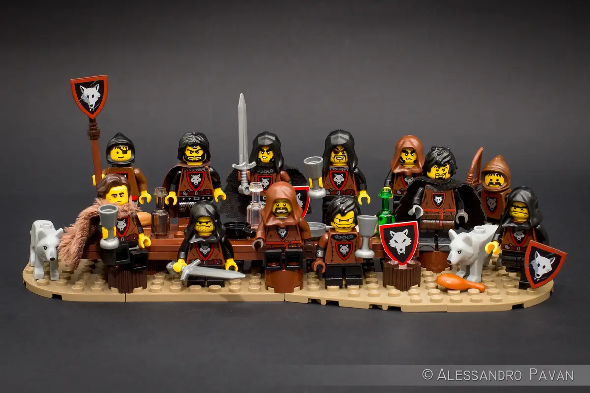 A group of Lego minifigures dressed as medieval warriors with wolf-themed heraldry, gathered around a table with goblets and…
