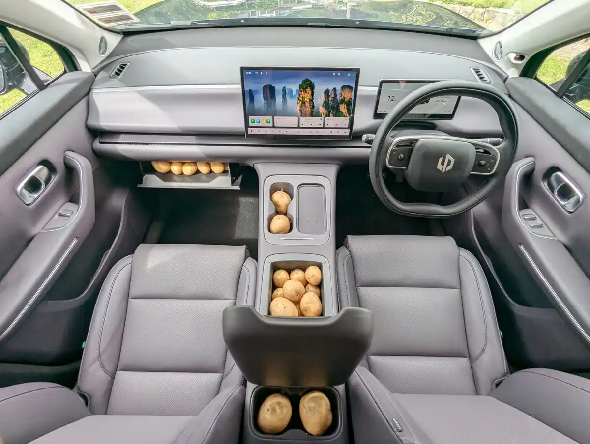 The interior of a modern car with a digital dashboard and steering wheel, filled with potatoes in multiple storage…