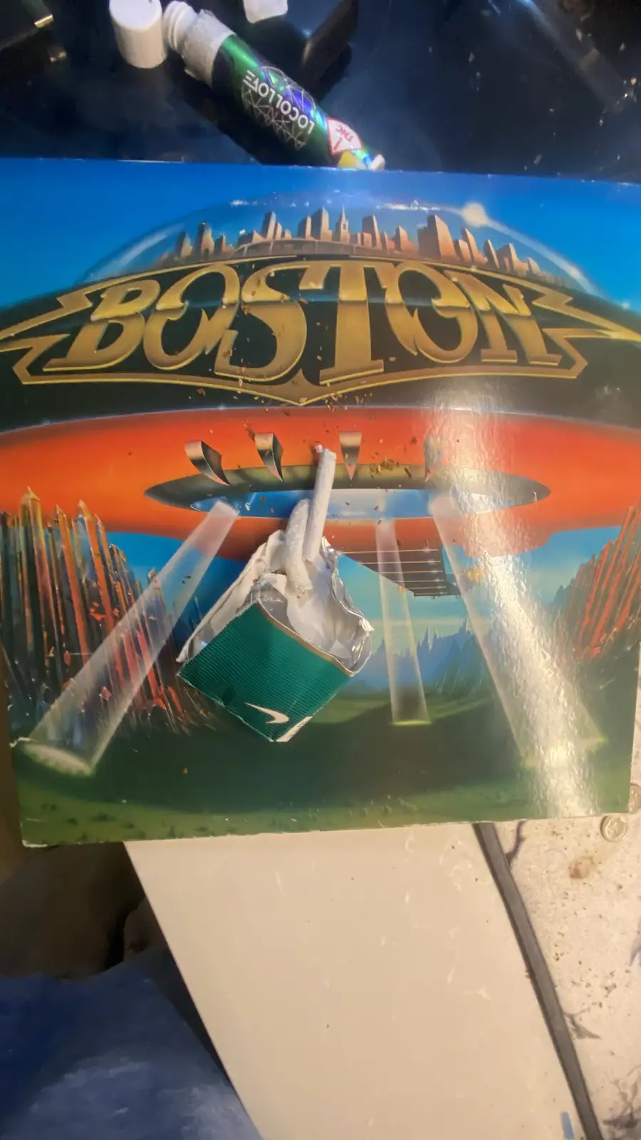 The image shows the iconic 'Boston' album cover art, which features a guitar and a city skyline. A real-life green…