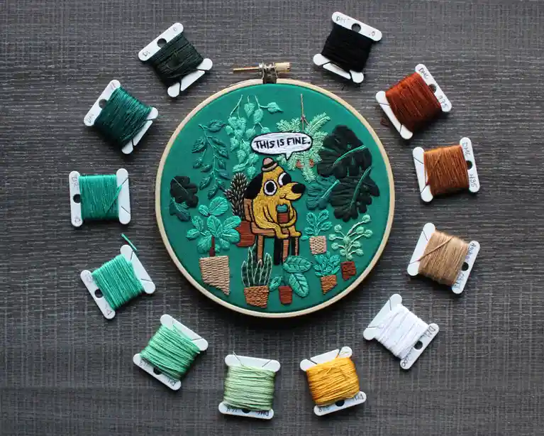 An embroidery hoop displays a stitched scene of a cartoon dog sitting among potted plants, with a speech bubble saying 'THIS…