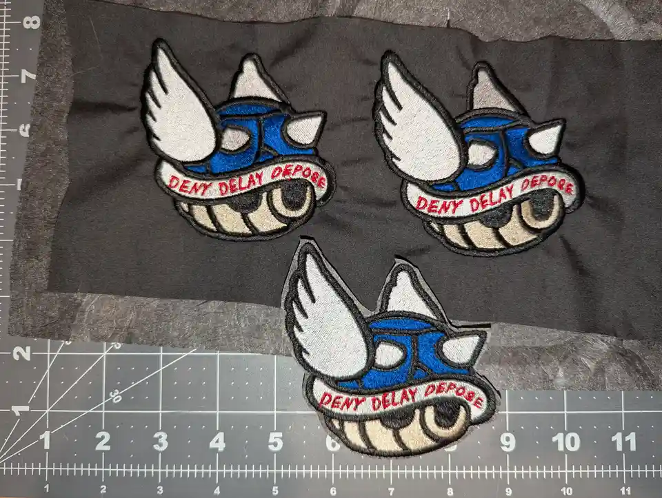 Three identical embroidered patches featuring a cartoonish blue and white winged fox-like creature with a wide grin and a…